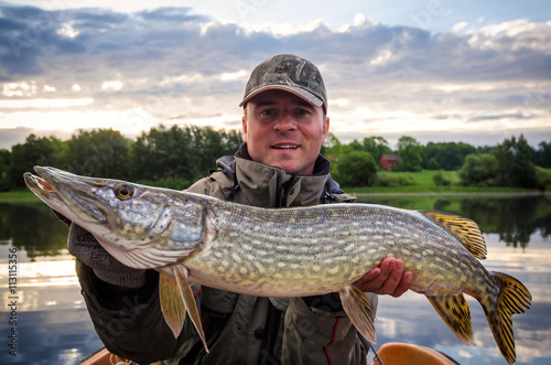 Happy angler with huge pike at morning time