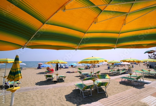 under the yellow with green stripes umbrella on the sunny beach photo