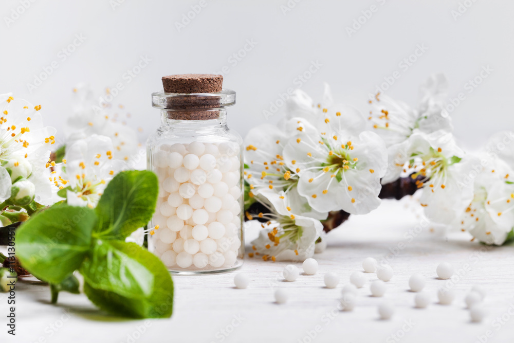 homeopathic pills with spring flowers on white background homeopathic pills with spring flowers on white background