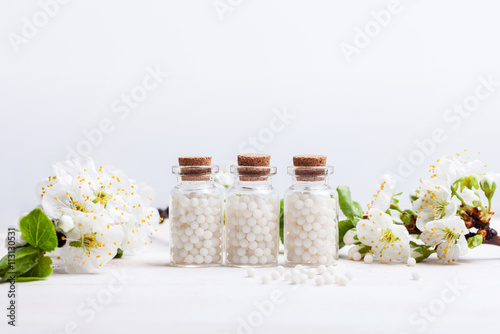 homeopathic pills with spring flowers on white background