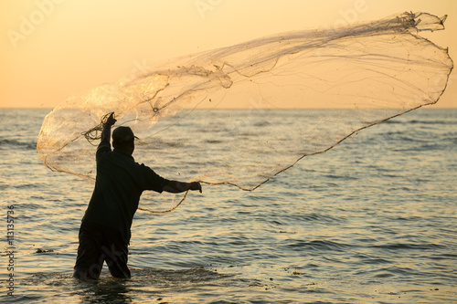 Silhouette of the unidentified Indian fisherman throwing net in sea on sunset in Fort Kochi, India. photo