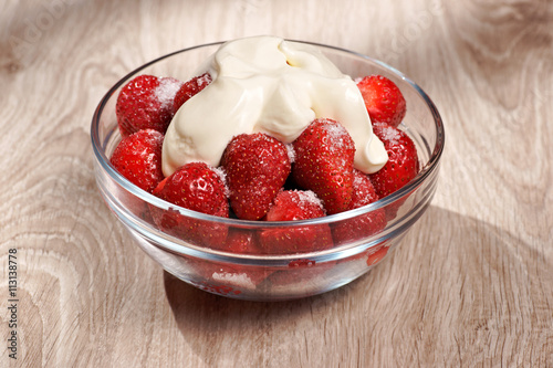 Strawberries with sugar and cream in a glass bowl on wooden table