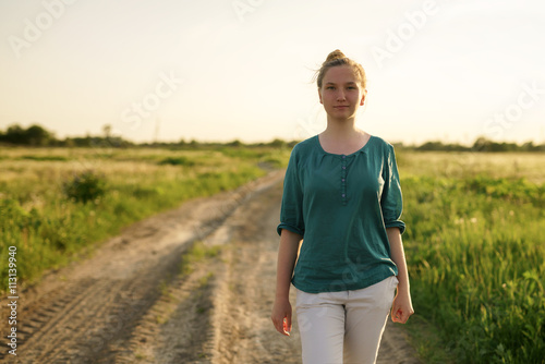 teen girl walking on dirt rural road between fields