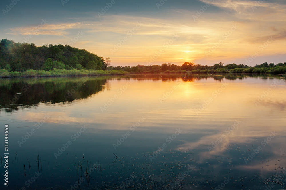 Beautiful summer sunset at the river with blue sky, red and orange clouds, green trees and water