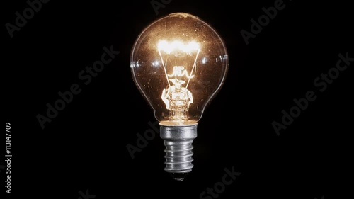 Lamp light bulb twinkles over black background, macro view, loop ready
