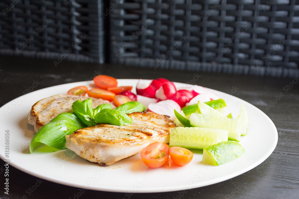 Pork steaks with vegetables on white plate on dark background Pork steaks with vegetables on white plate on dark background