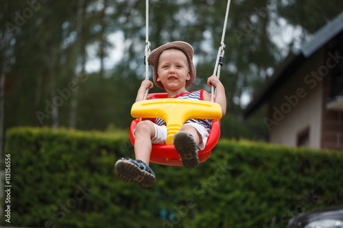 Little smiling  boy having fun and swinging on outdoor playgroun photo