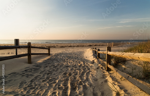 Wooden handrails on both sides  as the entrance to the sandy beach  footprints in the sand  waves and sky in the background Ocean city NJ
