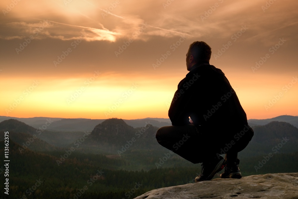 Short hair hiker in shirt sit on rock, enjoy foggy scenery