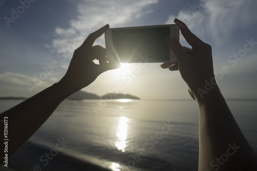 woman use smart phone take a photo of the sea and mountain in sunrise moment.