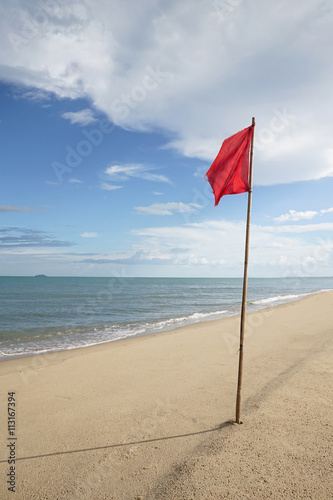 warning sign of a red flag at a beautiful clean beach with a blue sky and cloud in background