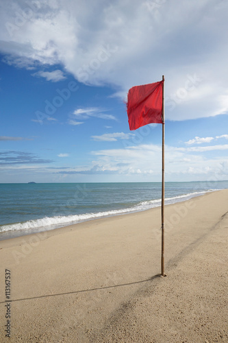 warning sign of a red flag at a beautiful clean beach with a blue sky and cloud in background