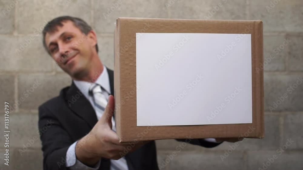Businessman waiting in a nice suit standing up against a wall holding a box that he hands to the viewer. Businessman waiting in a nice suit standing up against a wall holding a box that he hands to the viewer.
