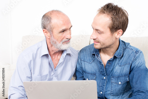 Elderly man with younger person surfing together in internet