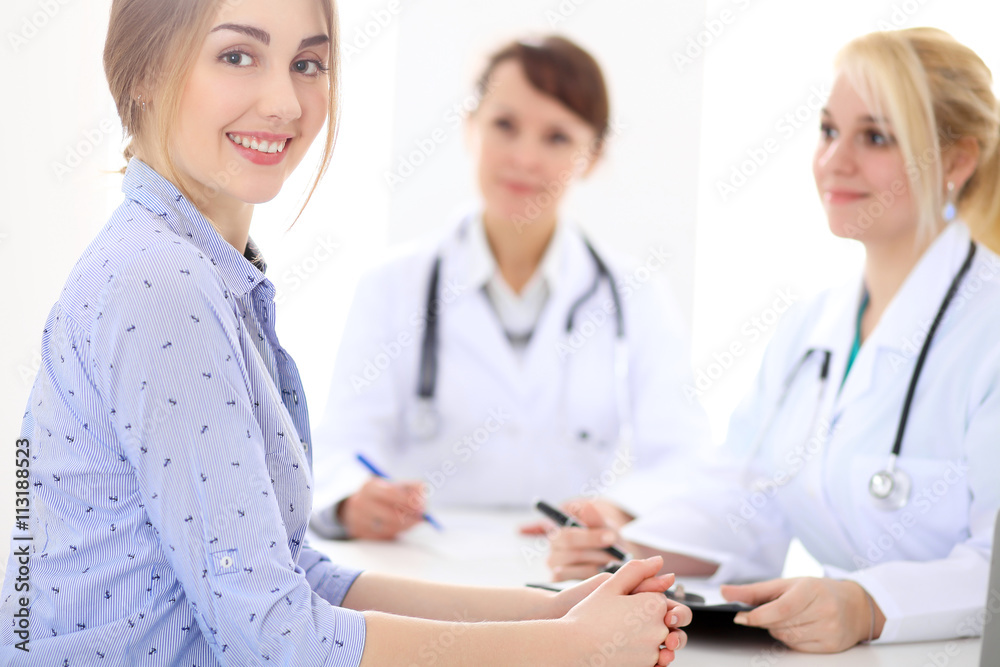 Happy smiling female patient with two cheerful doctors in the background. Medical and health care concept Happy smiling female patient with two cheerful doctors in the background. Medical and health care concept