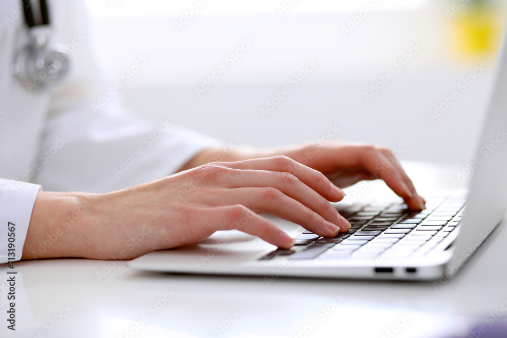Close-up of female doctor typing laptop sitting at a table in the hospital Close-up of female doctor typing laptop sitting at a table in the hospital