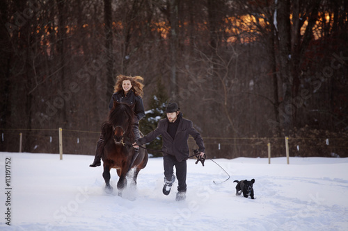 Woman riding horse, man and dog run alongside in a snowy landscape