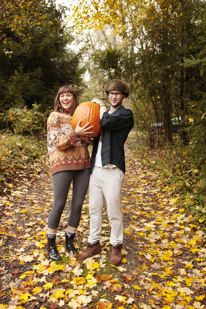Couple smiling while holding large pumpkin in autumn Couple smiling while holding large pumpkin in autumn