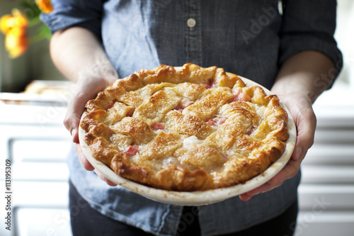 Midsection of woman holding baked rhubarb pie while standing at home photo