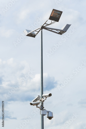 Four outside security cameras mounted on lamp post with cloudy sky