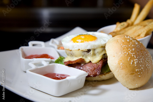 Gourmet Burger with Sunny-Side-Up Egg, Cheese, and Bacon.  A close-up view of a gourmet burger topped with a perfectly cooked sunny-side-up egg, melted cheese, and crispy bacon