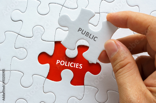 Hand holding piece of jigsaw puzzle with word PUBLIC POLICIES.