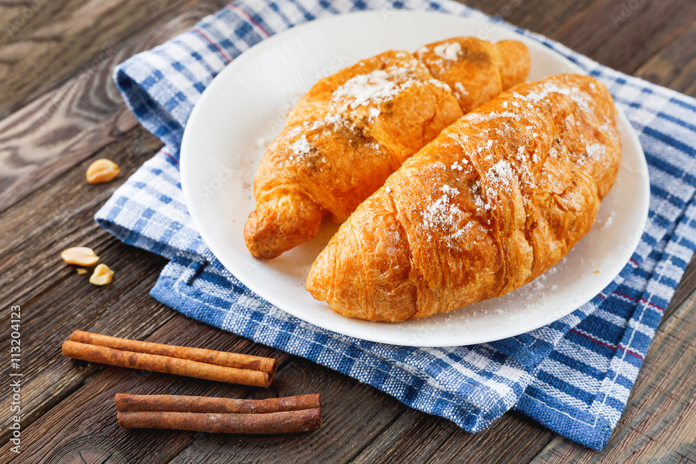 Continental breakfast background - pair of croissants with cinnamon on plaid blue napkin. Rustic wooden background.