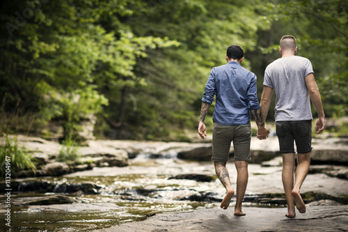 Rear view of gay couple walking near stream
