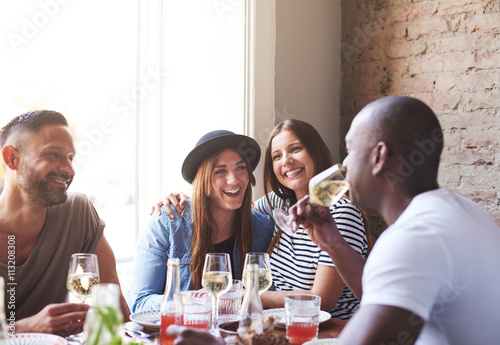 Photography Two ladies laughing while male friends drink wine
