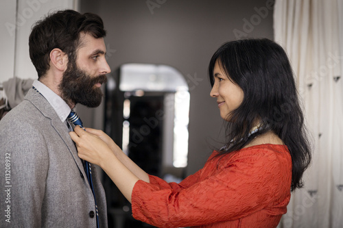Smiling woman adjusting necktie on husband at home