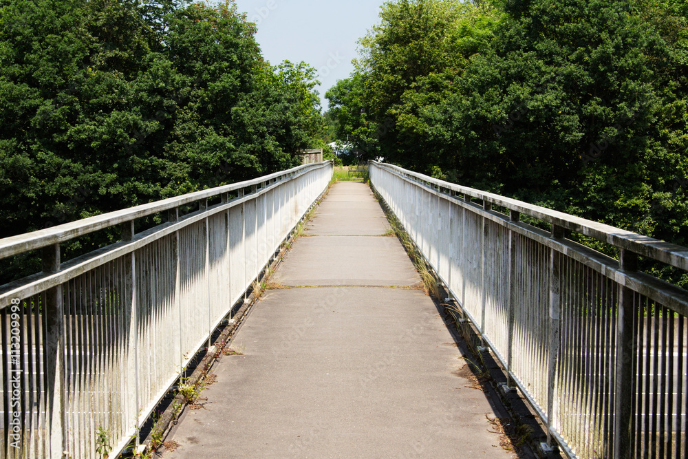 View along a long footbridge with railings on either side View along a long footbridge with railings on either side