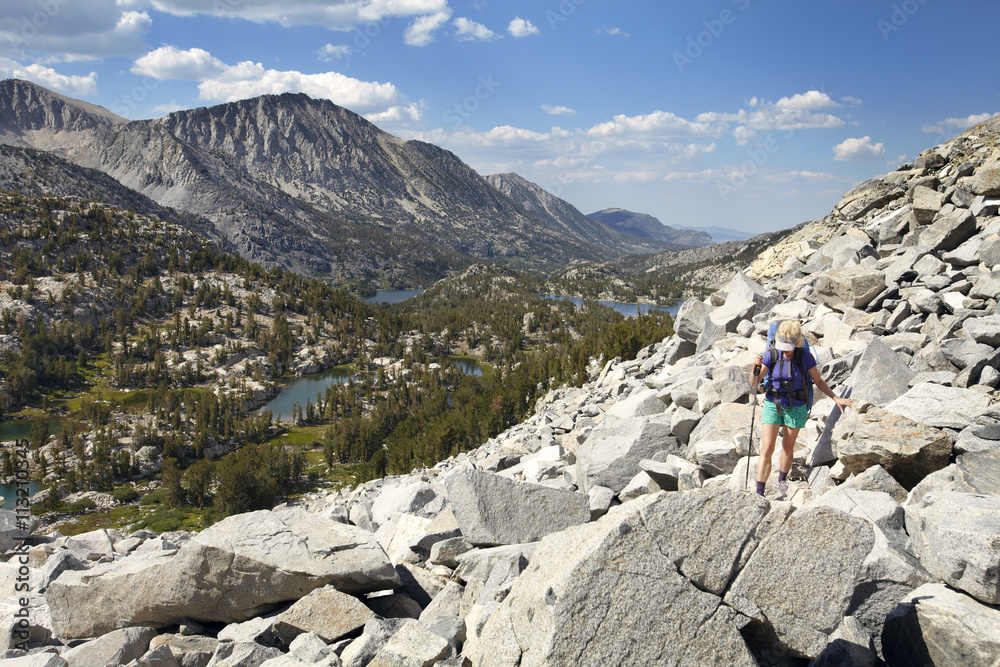 Hiker walking on rocks by mountains against sky Hiker walking on rocks by mountains against sky
