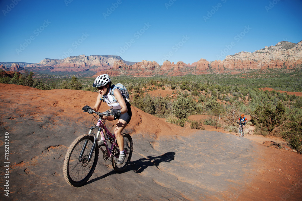 Friends riding bicycle on mountain against clear blue sky Friends riding bicycle on mountain against clear blue sky