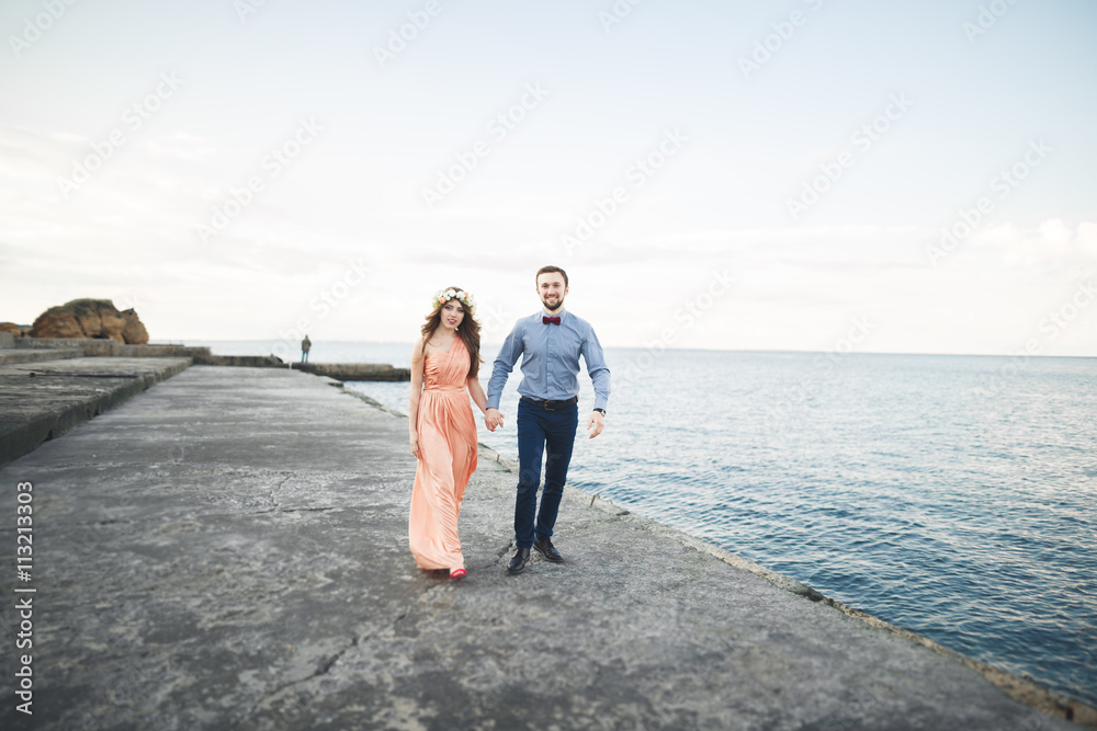 Beautiful loving couple, pride with long dress walking on pier Beautiful loving couple, pride with long dress walking on pier