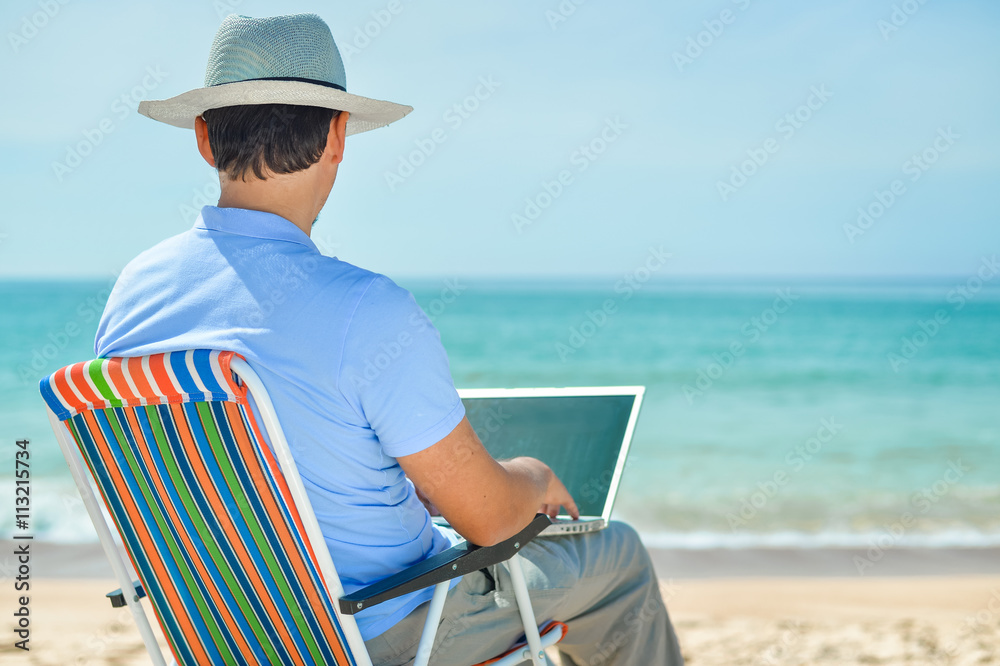 Back side view of relaxed man using laptop, beach background, outside summertime