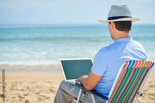 Business man using computer, tropical beach outdoors. Back view