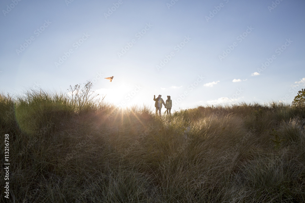 Couple flying kite while standing on field against sky Couple flying kite while standing on field against sky