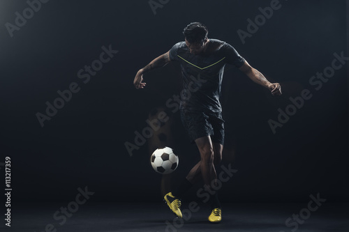 Young athlete playing soccer against black background photo