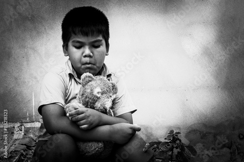Kid pauper with old teddy bear sitting near the concrete wall,bl