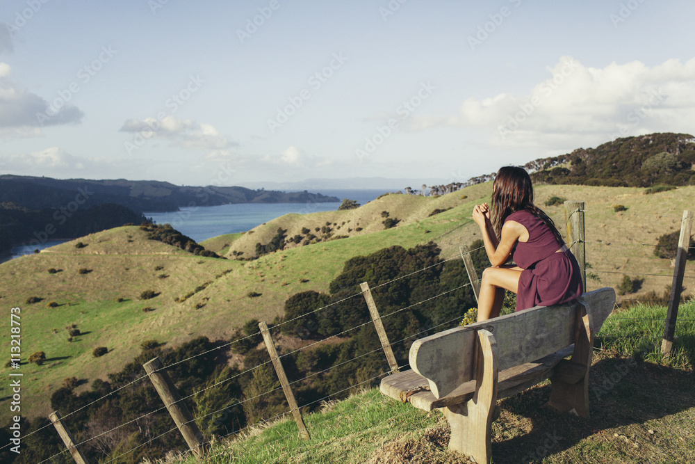 Woman sitting on bench, looking at coastline Woman sitting on bench, looking at coastline