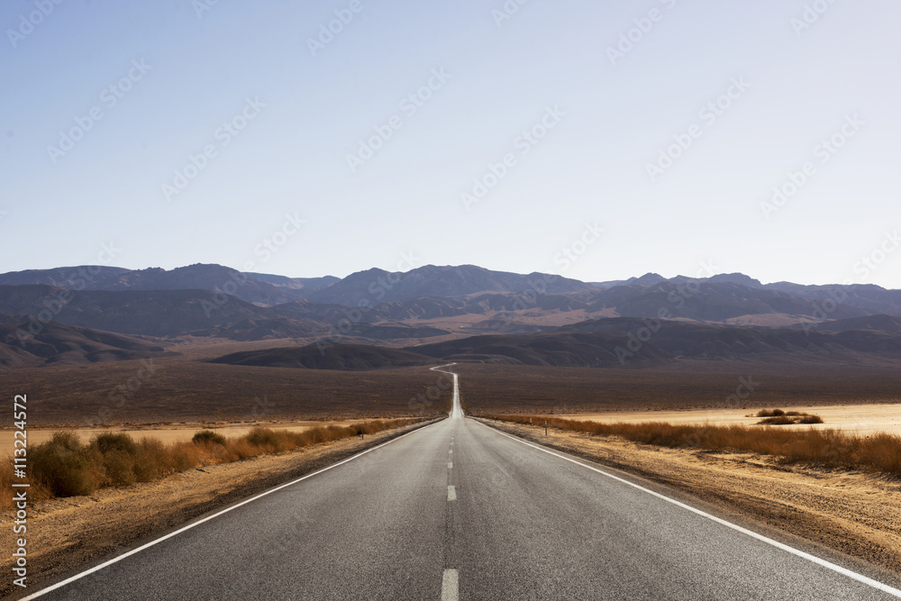 Empty country road amidst field against mountains and clear sky Empty country road amidst field against mountains and clear sky