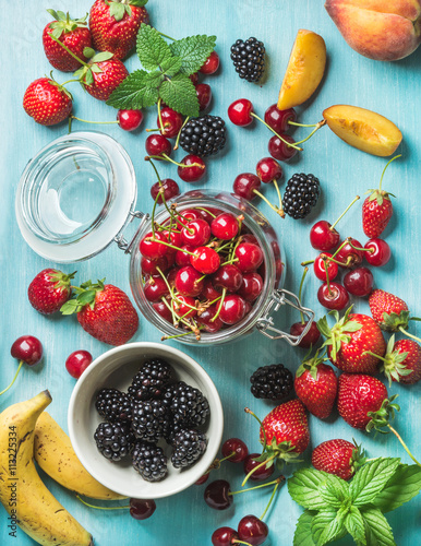 Healthy summer fruit variety. Sweet cherries  strawberries  blackberries  peaches  bananas and mint leaves on blue backdrop