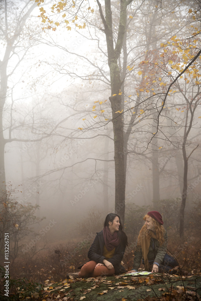 Smiling friends with map talking while sitting in forest Smiling friends with map talking while sitting in forest