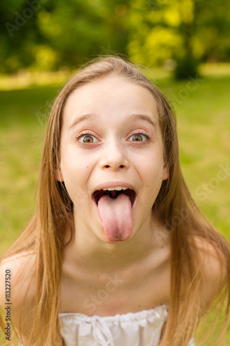Outdoors portrait of beautiful young girl looking at you and showing tongue