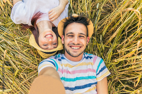 Young caucasian couple taking selfie lying on the grass.