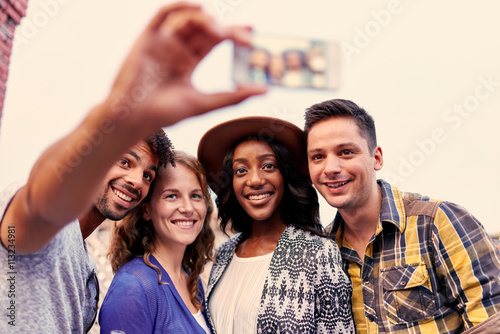 Multi-ethnic millenial group of friends taking a selfie photo with mobile phone on rooftop terrasse at sunset photo
