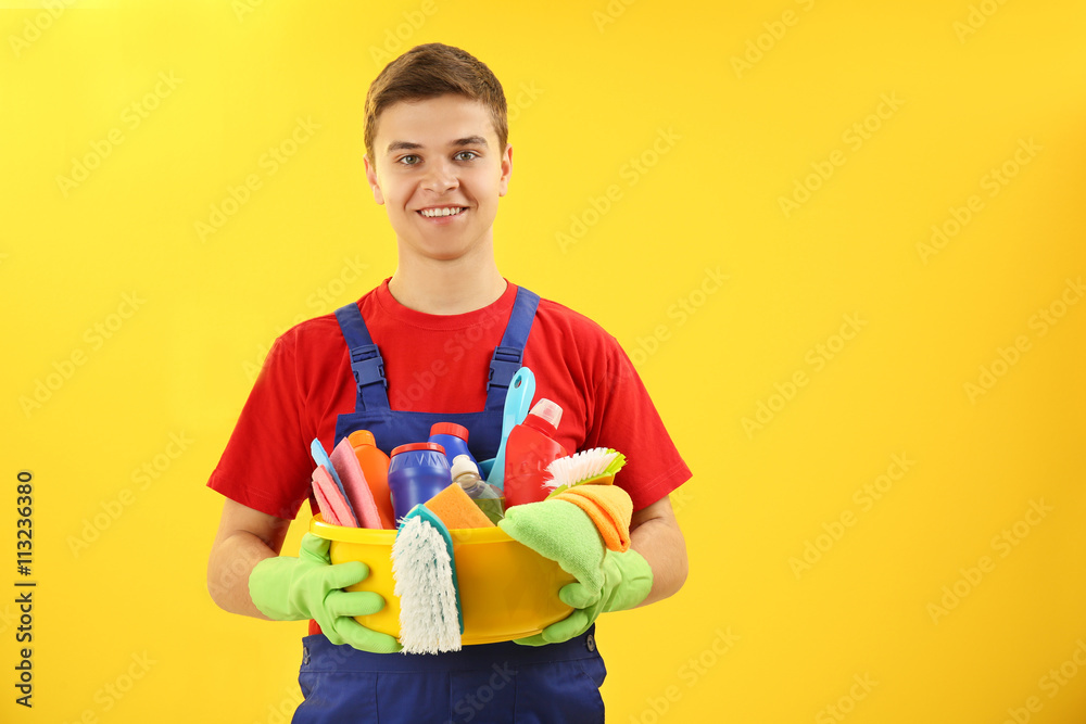 Man holding plastic basin with brushes, gloves and detergents on yellow background