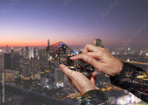 Double exposure of woman hand touch screen smart phone, tablet,cellphone and night cityscape as technology and communication concept.