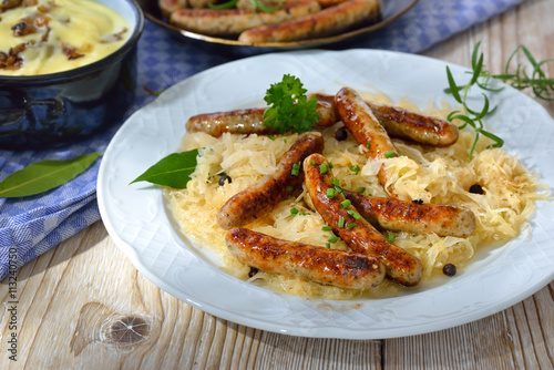 Deftige, gebratene Rostbratwürstchen auf Sauerkraut mit Kartoffelpüree serviert - Fried Bavarian sausages from Nuremberg on sauerkraut served with mashed potatoes