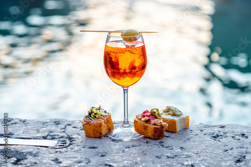 Fototapeta Spritz Aperol drink with venetian traditional snacks cicchetti on the water chanal background in Venice
